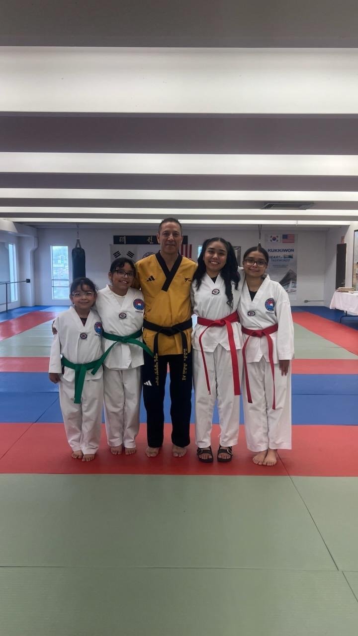 Master Marcelo Sanchez in gold dobok with students showing green and red belts on colorful dojo mats