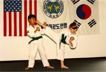 Two children sparring in Taekwondo class with flags in background